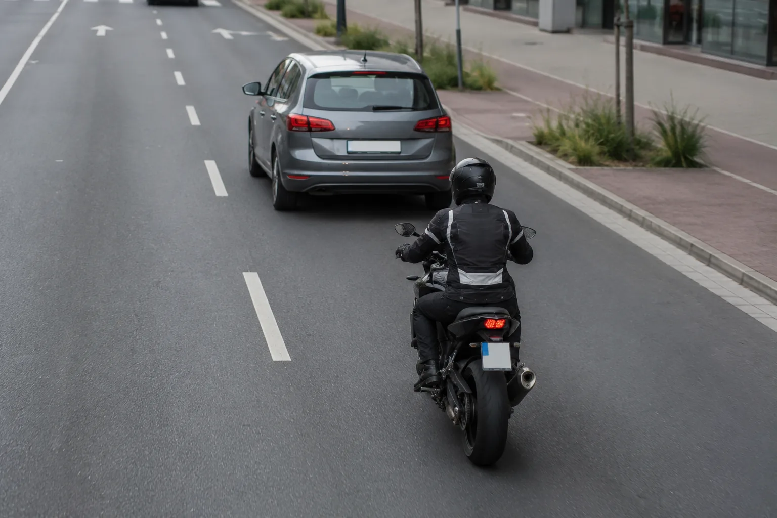 Motorrad fährt versetzt und mit Abstand hinter einem Pkw auf einer mehrspurigen Straße.