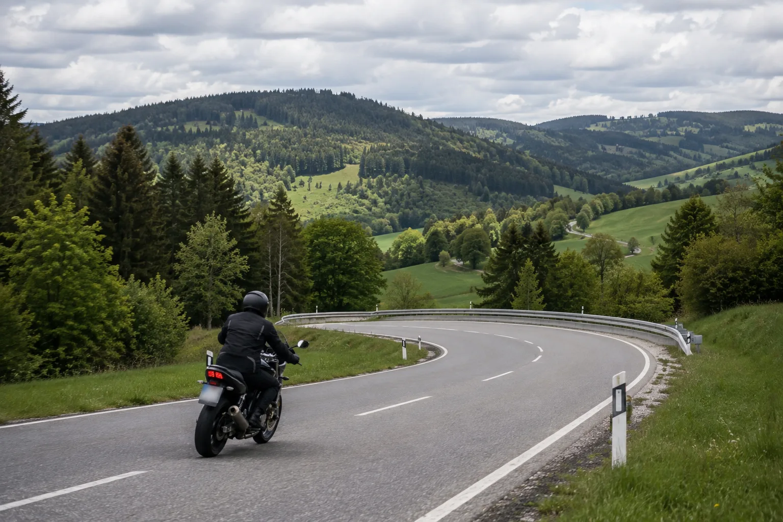 Motorradfahrerin auf einer übersichtlichen kurvigen Landstraße in einer Mittelgebirgslandschaft
